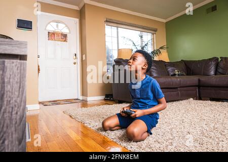 Ragazzo che gioca a un videogioco mentre si siede sul tappeto a casa Foto Stock
