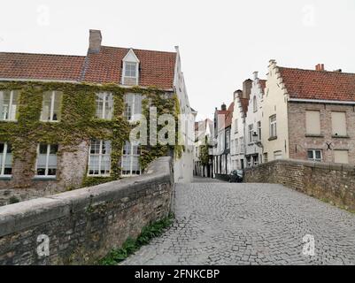 Vista classica di un ponte acciottolato che conduce in una strada laterale circondata da tradizionali case in stile a groviglio a gradini a Groenerei, Bruges, Belgio Foto Stock