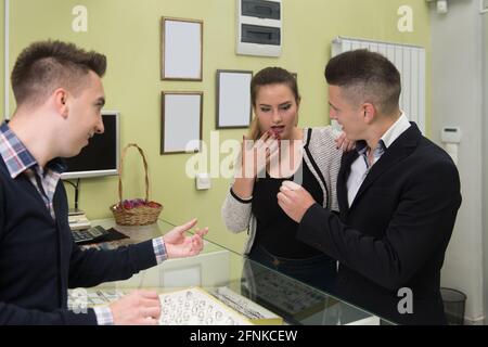 Attraente giovane coppia che esamina selezione degli anelli mentre il suo amore Boyfriend in piedi presso il negozio di gioielli Foto Stock