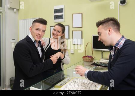 Attraente giovane coppia che esamina selezione degli anelli mentre il suo amore Boyfriend in piedi presso il negozio di gioielli Foto Stock