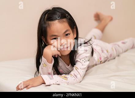 Bella ragazza asiatica in pigiama, sdraiata sul letto e appoggiata sul braccio. Foto Stock