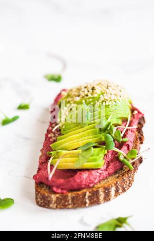 Brindisi con hummus di barbabietola e avocado, sfondo di marmo bianco. Concetto di cibo vegano. Foto Stock