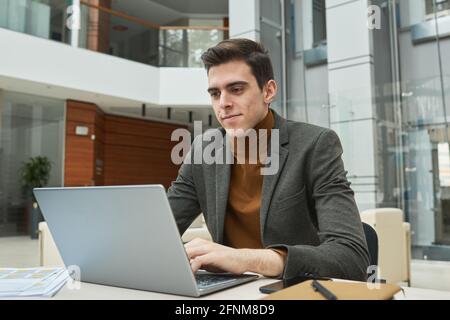Giovane uomo d'affari serio che lavora su un computer portatile sul suo posto di lavoro ufficio Foto Stock