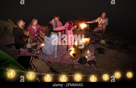 Giovani amici hippie divertirsi insieme durante la festa notturna sulla spiaggia Con luce a corda - concetto di viaggio amicizia con i giovani viaggiatore che beve birra Foto Stock