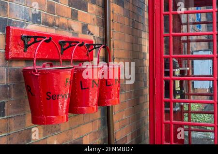 Tre secchielli antincendio rossi contro un chiosco telefonico rosso sulla piattaforma alla stazione di Quorn & Woodhouse, Great Central Railway, Regno Unito Foto Stock