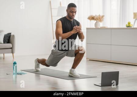 Black Guy facendo Forward Lunge esercizio su laptop a casa Foto Stock