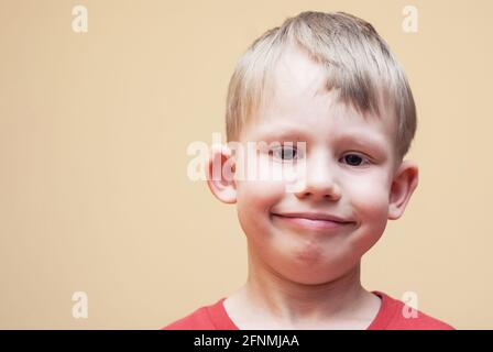 Ritratto di ragazzo sorridente con occhi marroni in abito rosso posa per la fotocamera su sfondo beige in studio vista ravvicinata Foto Stock