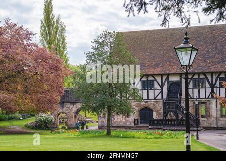 Un antico edificio a graticcio situato in un parco comunale. Una lampada è in primo piano e un prato si estende di fronte se l'edificio. Foto Stock