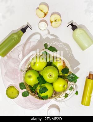 Composizione cosmetica verticale con mele verdi, bottiglie di plastica con crema, lozione, gel, scrub, sapone su fondo bianco. Prodotti di bellezza estivi Foto Stock