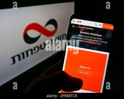 Persona che detiene cellulare con pagina web della società finanziaria israeliana Mizrahi-Tefahot Banca sullo schermo di fronte al logo. Mettere a fuoco il centro del display del telefono. Foto Stock