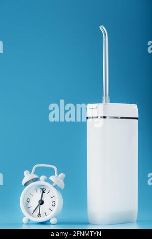 Pulizia orale con irrigatore con sveglia su sfondo blu. Un dispositivo mobile per spazzolare i denti e un sorriso bianco neve. Spazio libero Foto Stock