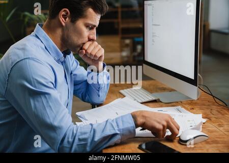 Giovane uomo d'affari pensivo che lavora con i documenti mentre si siede in ufficio. Imprenditore di successo sta studiando documenti con attenzione e concentrazione Foto Stock