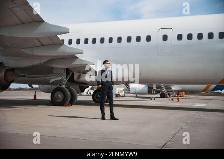 Pilota maschile che riposa di fronte all'aereo Foto Stock