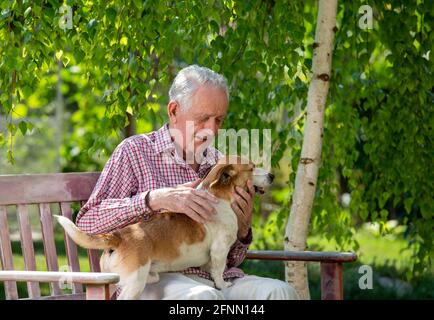 Uomo anziano seduto in giardino con cane carino in giro e coccolarsi Foto Stock