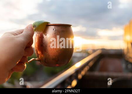 Un mule di mosca tenuto in su ad un bar ristorante sul tetto al tramonto Foto Stock