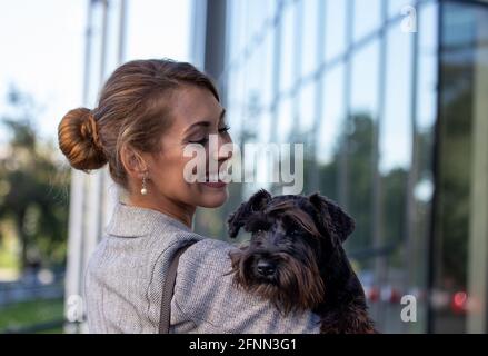 Bella giovane donna di affari che tiene il cane carino in armi dentro davanti all'edificio degli uffici