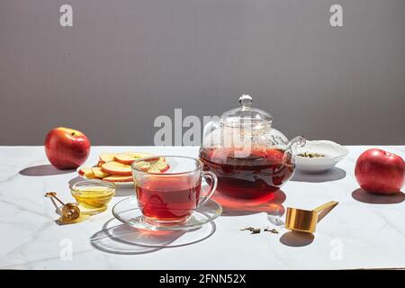 Tè alla frutta con mele e timo e miele in teiera di vetro e tazza su sfondo bianco con ombre dure. Foto Stock