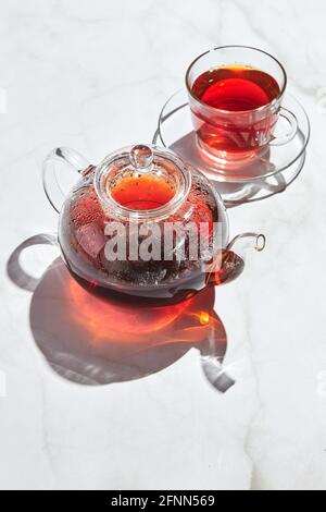 Tè alla frutta con mele e timo e miele in teiera di vetro e tazza su sfondo bianco con ombre dure. Foto Stock
