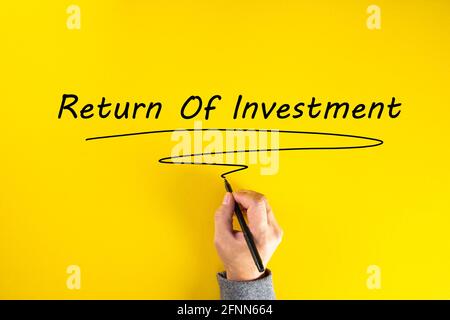 Mano di uomo d'affari che scrive ritorno sull'investimento su sfondo giallo. Foto Stock