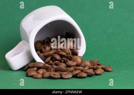 Tazza bianca capovolta di caffè con chicchi di caffè tostati all'interno su sfondo verde Foto Stock