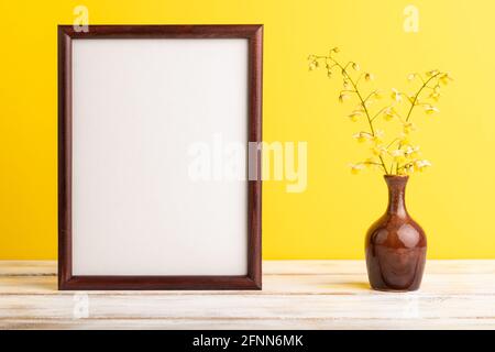 Cornice in legno con fiori gialli barrenwort in vaso ceramico su sfondo giallo pastello. Vista laterale, spazio copia, vita still, mockup, dima, molla, Foto Stock