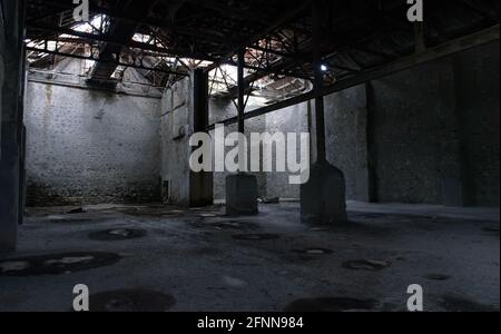 Backgdrop industriale. Abbandonato magazzino vuoto con pareti in pietra, tetto rotto e colonne arrugginite Foto Stock