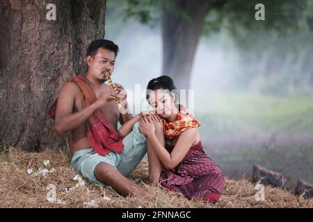 Coppia amore di giovani asiatici e donne seduti sotto l'albero contro bufali e sfondo naturale, stile di vita rurale nel nord-est della Thailandia. R Foto Stock
