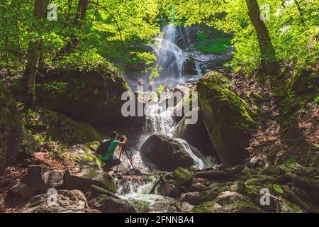 Il fotografo viaggiatore scatta foto di una cascata nella foresta verde Foto Stock