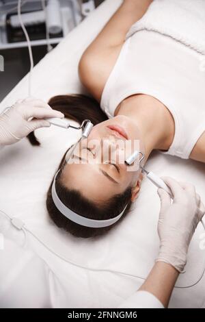 Trattamento galvanico della pelle e concetto di clinica di bellezza. Cosmetologo estetista mani in guanti facendo viso al cliente faccia. Il medico esegue la galvanica Foto Stock