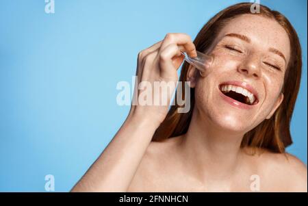 Cura della pelle. Donna felice che fa massaggio di cupping facciale a casa, usando ventosa a vuoto e ridendo, sorridente denti bianchi. Ragazza redhead lifting Foto Stock