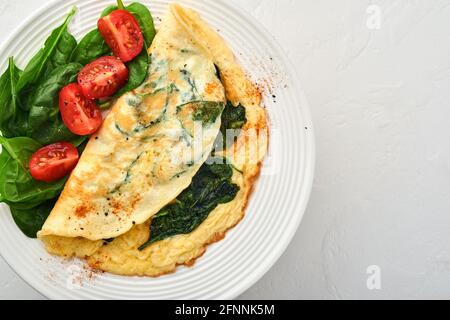 Omelette o omelette con spinaci, pomodoro di ciliegia e pepe su un piatto bianco, su fondo bianco. Vista dall'alto. Foto Stock