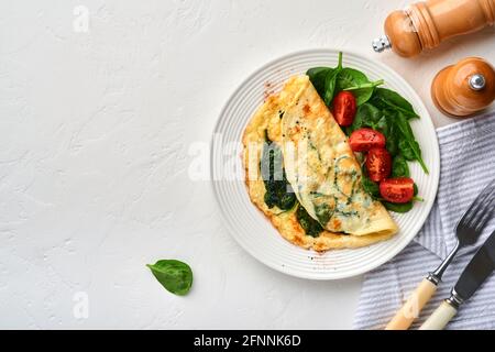 Omelette o omelette con spinaci, pomodoro di ciliegia e pepe su un piatto bianco, su fondo bianco. Vista dall'alto. Foto Stock