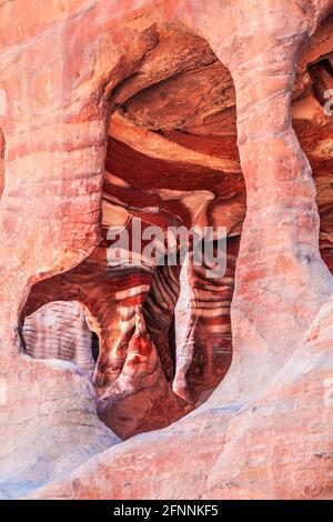 Vista attraverso una delle aperture nella strada delle facciate di Petra, Giordania, che mostra gli strati di arenaria rossa. Foto Stock
