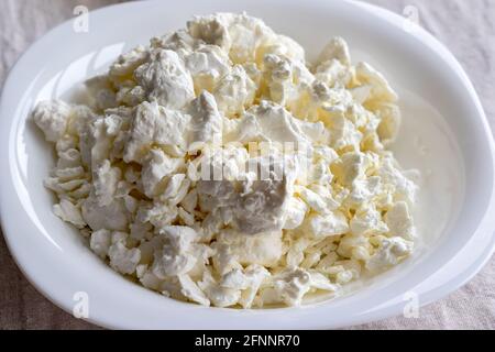 Un piatto bianco riempito con formaggio di cottage su una tovaglia di lino. Vista in primo piano. Messa a fuoco selettiva Foto Stock