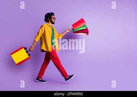 Foto a tutta lunghezza di un bell'abbigliamento di pelle scura positivo maglietta gialla capo camminare shopping isolato viola sfondo colore Foto Stock