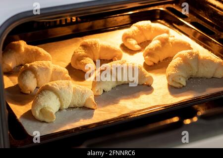 Croissant ghiacciati al forno su una teglia ricoperta di carta pergamena. Bagel dolci da un impasto di formaggio cotto in un forno caldo. Il Foto Stock