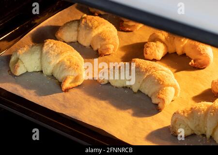 Croissant ghiacciati al forno su una teglia ricoperta di carta pergamena. Bagel dolci da un impasto di formaggio cotto in un forno caldo. Il Foto Stock