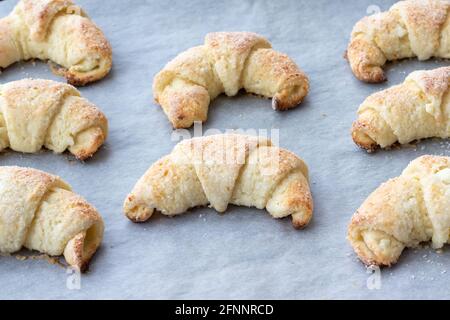 Croissant cotti da un impasto di formaggio casolare con zucchero su una teglia con carta pergamena appena tolto dal forno. Spuntino a base di tè per colazione. Th Foto Stock