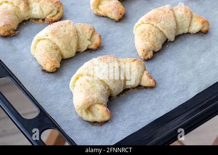 Croissant cotti da un impasto di formaggio casolare con zucchero su una teglia con carta pergamena appena tolto dal forno. Spuntino a base di tè per colazione. Th Foto Stock