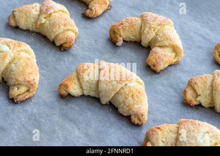 Croissant cotti da un impasto di formaggio casolare con zucchero su una teglia con carta pergamena appena tolto dal forno. Spuntino a base di tè per colazione. Th Foto Stock