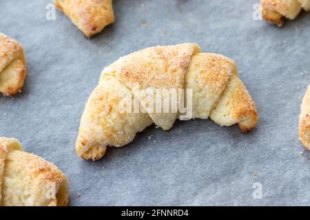 Croissant cotti da un impasto di formaggio casolare con zucchero su una teglia con carta pergamena appena tolto dal forno. Spuntino a base di tè per colazione. Th Foto Stock