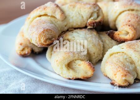 Croissant da un impasto casolare di formaggio su un piatto bianco su una tovaglia di lino grigio appena tolto dal forno. Il processo di fabbricazione dei bagels cagliati o cr Foto Stock