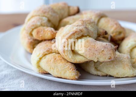 Croissant ghiacciati da un impasto di formaggio su un piatto bianco su una tovaglia di lino grigio appena tolto dal forno. Spuntino a base di tè per colazione. Foto Stock