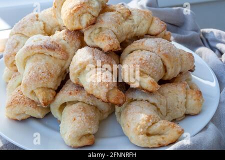 Croissant ruddy ghiacciati da un impasto di cagliata adagiato su un piatto bianco accanto a un panno grigio. I bagel appena sfornati sono appena tolti dal forno. Un delicio Foto Stock