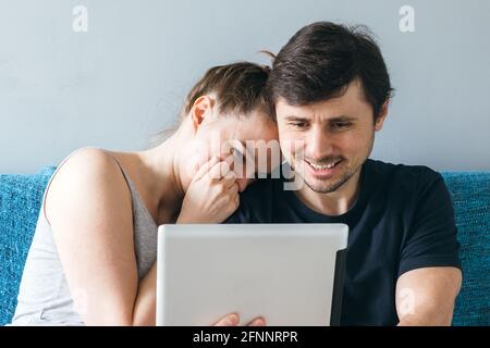 Una coppia sposata sorridente si diverte a parlare con genitori o amici tramite una chiamata online tramite tablet. Un uomo e una donna, una famiglia di due, fare una videochiamata o. Foto Stock