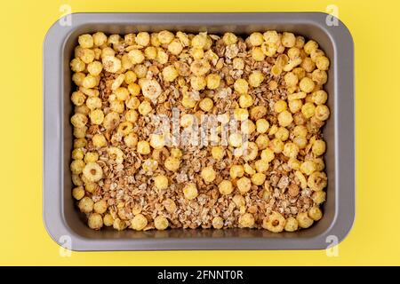 Cereali croccanti biologici fatti in casa con farinata d'avena e semi di lino fiocchi e palle di mais croccanti e anelli nella teglia da forno su sfondo giallo brillante Foto Stock