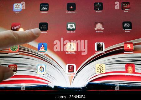 Uomo che legge un iPad tablet digitale con varie applicazioni digitali religiose. Cristianesimo, Islam, Giudaismo, Buddismo. Simboli interreligiosi. Francia. Foto Stock