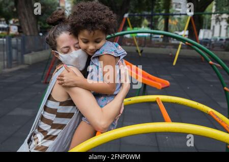 Madre e figlia si abbracciano al parco giochi all'aperto nella vita pandemica Foto Stock