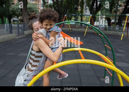 Madre e figlia si abbracciano al parco giochi all'aperto nella vita pandemica Foto Stock