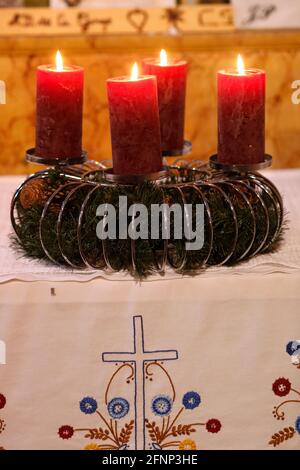 Corona o corona dell'avvento naturale in una chiesa cattolica con quattro candele rosse brucianti. Francia. Foto Stock